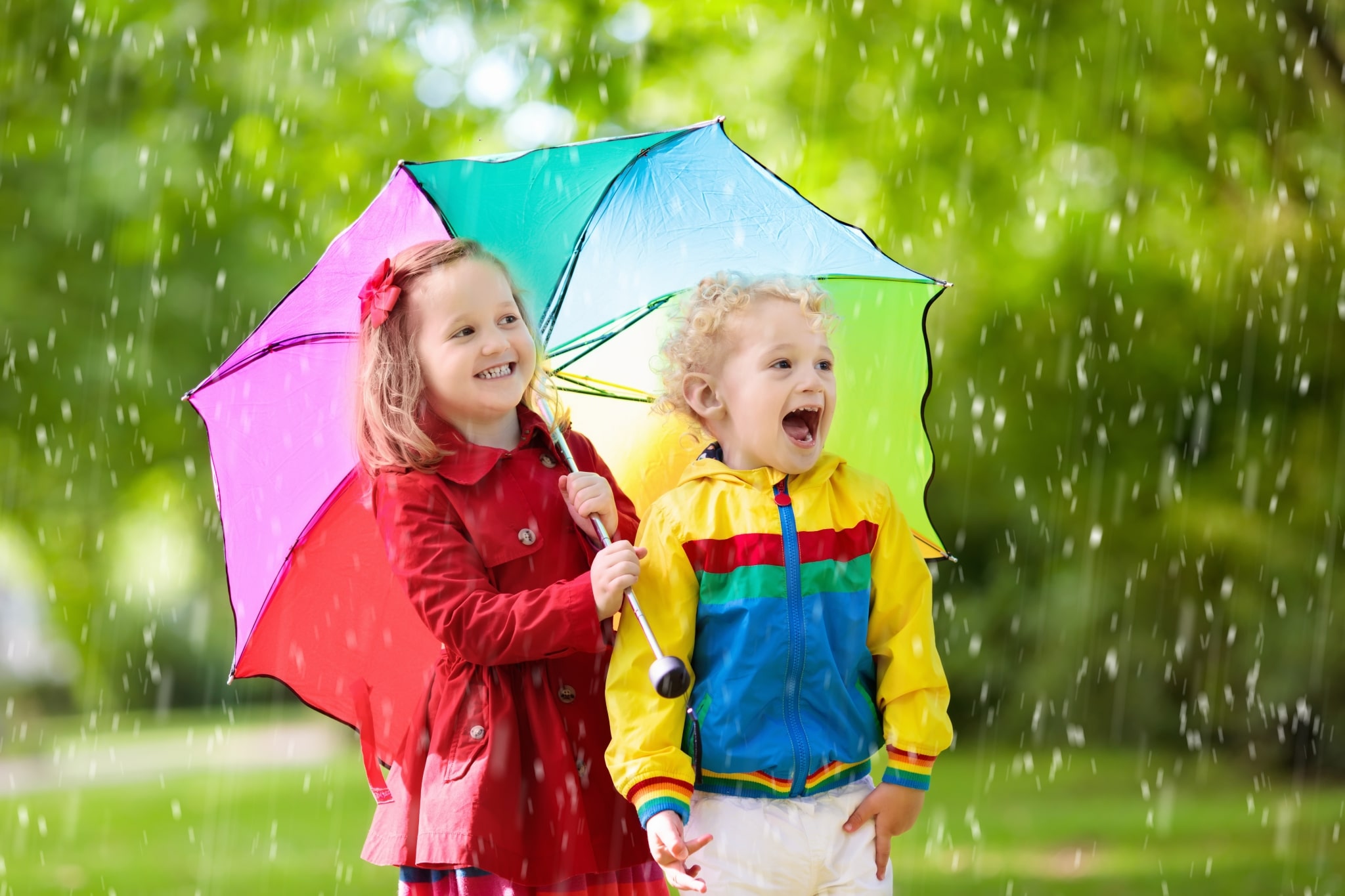 Kids playing in the rain under colorful umbrella