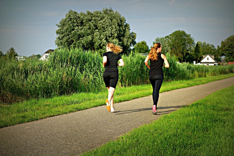 Sie sehen zwei junge Frauen beim Joggen auf einem Weg im Grünen